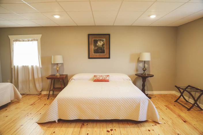 Cozy bedroom with a centered bed, nightstands, lamps, framed art, and wooden floors