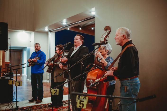 Four musicians perform indoors with violins, cello, and microphones on stands.