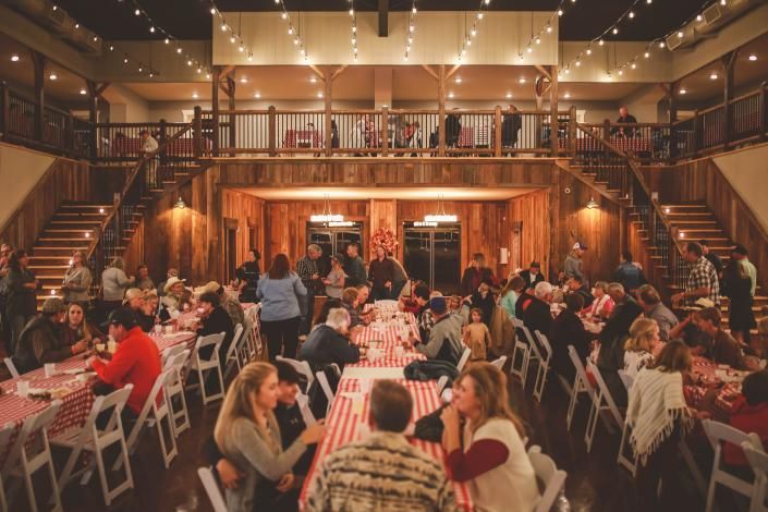 Indoor wedding reception with guests dining at long tables under warm string lights in a rustic hall