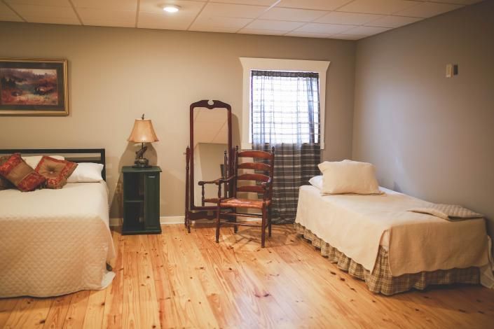 Spare bedroom with two twin beds, wooden floor, lamp, mirror, and window with curtain.
