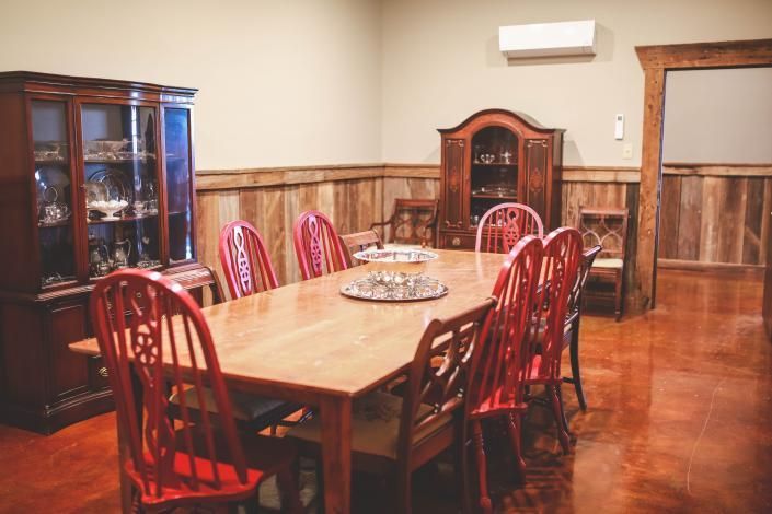 Wood-paneled dining room with a long wooden table, red chairs, and glass display cabinets