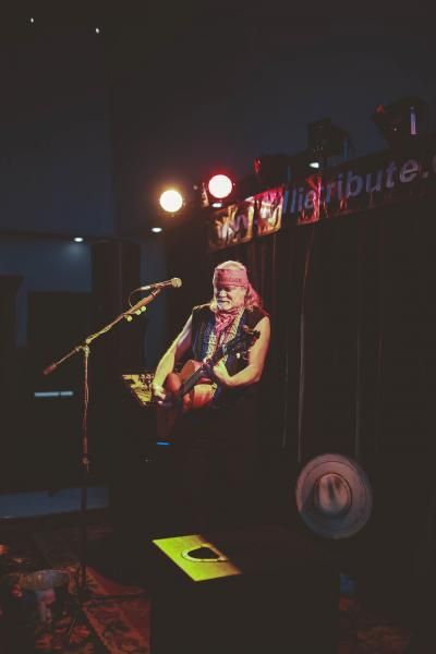 Musician playing guitar on a dimly lit stage under red and white lights
