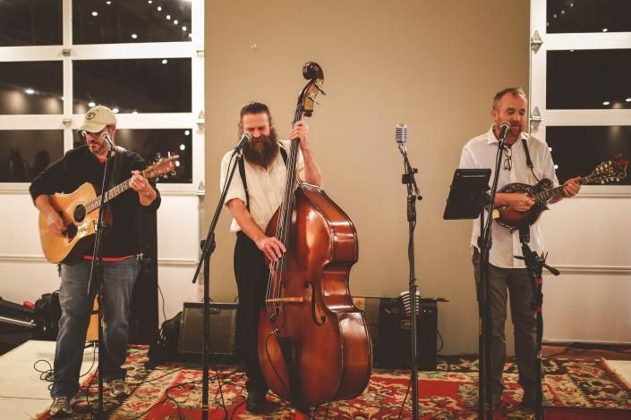 Three musicians playing acoustic instruments at a live indoor performance on a rug-covered floor