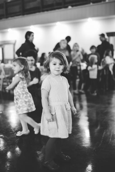 Children dancing at an indoor event, with one child in a light dress in the foreground.