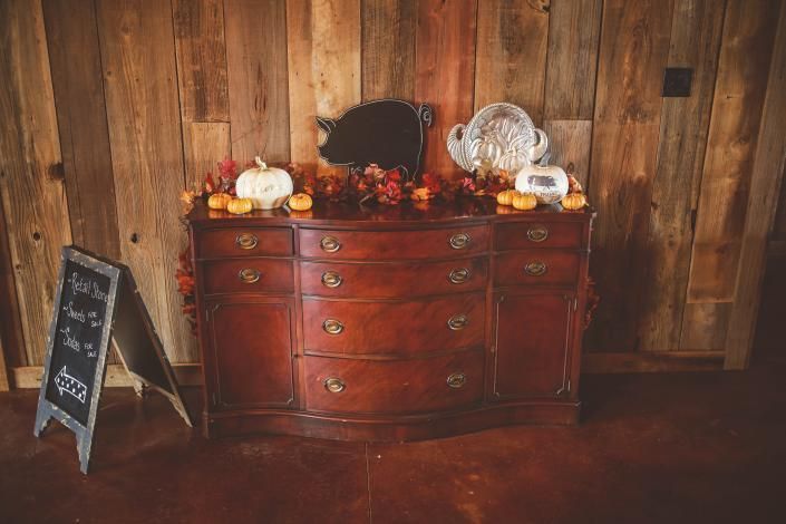 Rustic wooden dresser with fall decor, flowers, pumpkins, and a chalkboard sign against a wood wall.