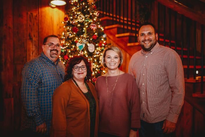Four people smiling in a warmly lit indoor venue with red curtains and string lights.