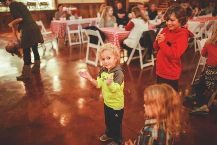Children dancing in a warmly lit room with tables and chairs in the background