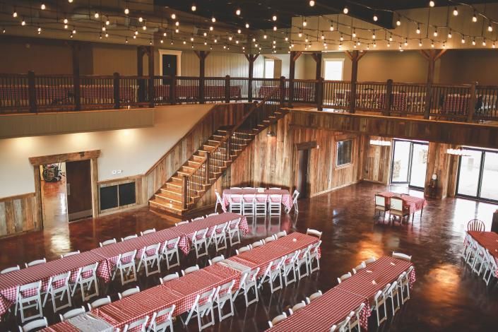 Decorated banquet hall with long tables, white chairs, string lights, and a staircase balcony