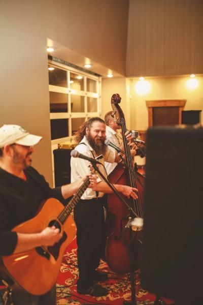 Three musicians perform indoors, with guitars and an upright bass under warm lights.