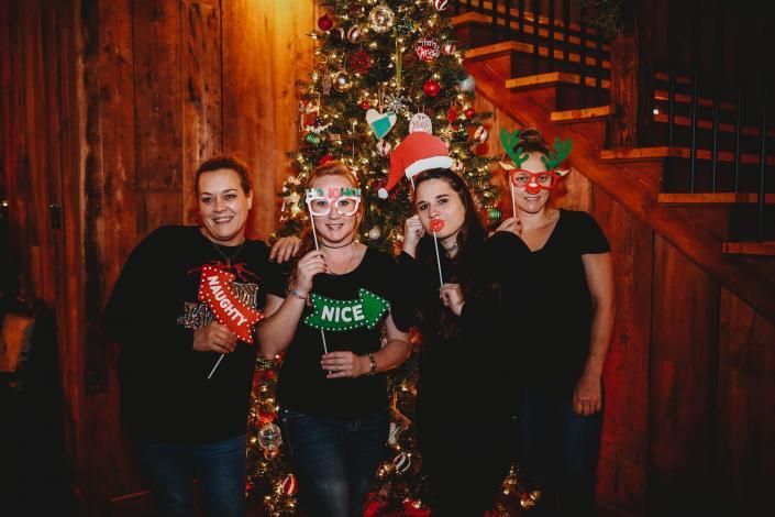 Four people in festive holiday outfits posing by a decorated Christmas tree indoors