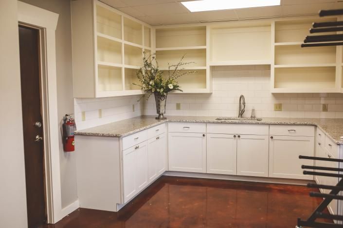 Empty beige kitchen with white cabinets, countertop sink, open shelving, and terracotta tile floor