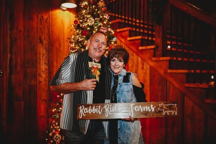 Smiling couple holding a wooden sign in front of a warm-lit staircase and wooden wall