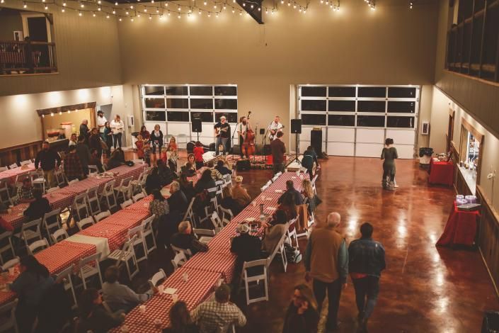 Indoor event hall with rows of red chairs, people mingling, and string lights overhead