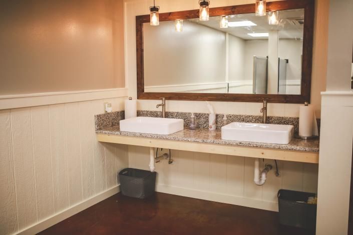Restroom vanity with two sinks, large mirror, and warm pendant lights over a tiled counter.