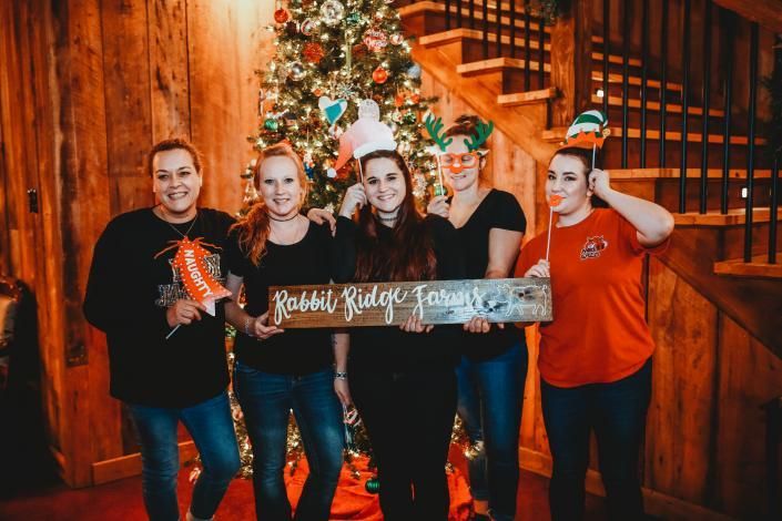 Five people holding a festive holiday sign in front of a decorated Christmas tree and wooden staircase