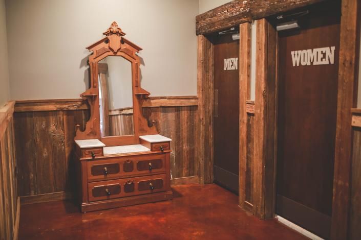 Wood-paneled restroom with a vanity mirror and two stalls labeled MEN and WOMEN
