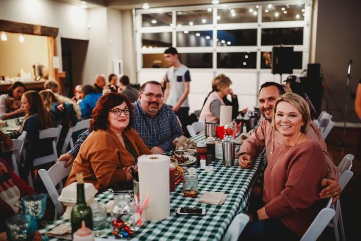 Friends seated at a checkered table in a warmly lit restaurant, smiling during a group meal