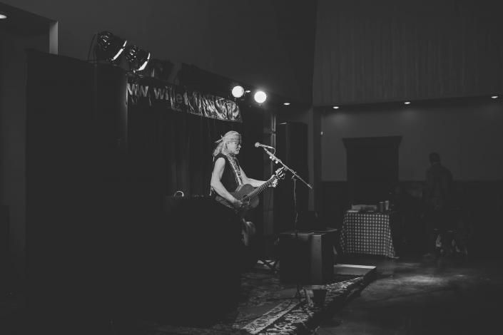 Solo guitarist performs on a dimly lit stage with spotlights and a microphone stand.