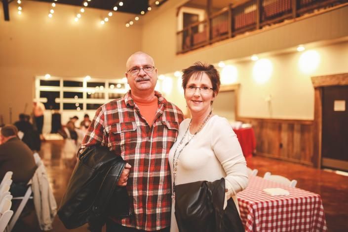 Two people standing together in a warmly lit hall, smiling at the camera.