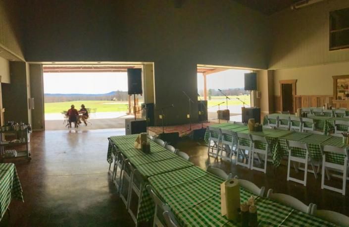 Indoor dining hall with checkered tables and chairs, open doorway to a bright outdoor view, two people walking outside