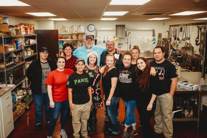 Group of people posing together in a workshop, with tools, shelves, and equipment in the background.