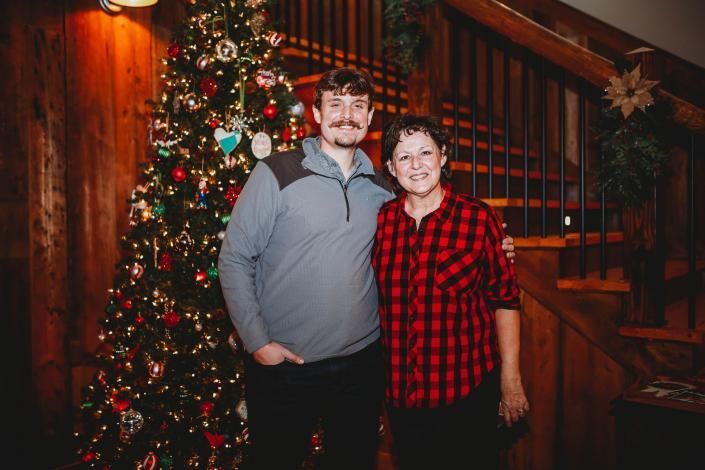 Two people standing beside a decorated Christmas tree indoors, smiling at the camera.