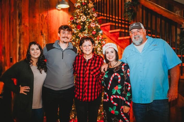 Five people posing in front of a decorated Christmas tree in a cozy indoor setting