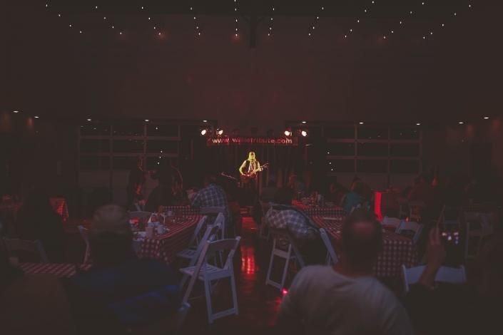 Dimly lit outdoor event with red lighting, tables, chairs, and a lit stage in the center.