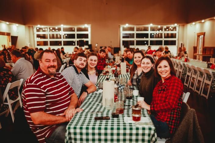 People seated at a long banquet table in a dining hall, smiling and raising drinks