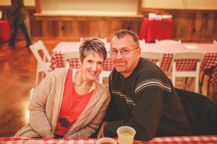Two smiling people seated together at a table in a warmly lit café or banquet hall