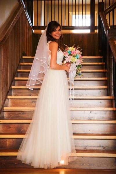 Bride in a white gown holding a bouquet, smiling on a staircase with wooden railings