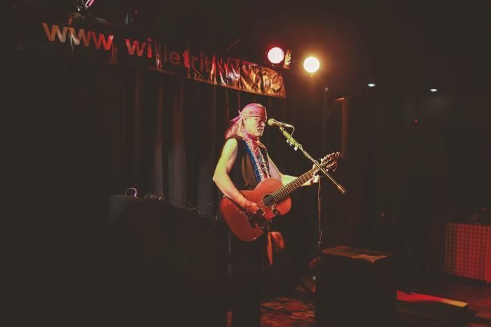 Singer performing on a dark stage with a red guitar under warm lights