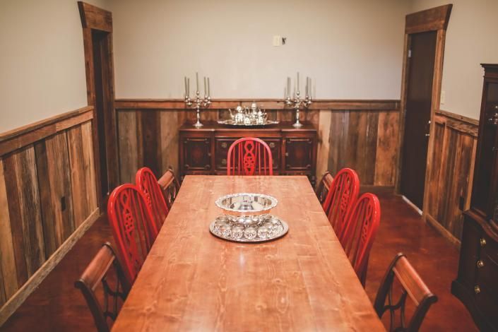 Long wooden dining table with red chairs in a rustic room, set with decorative plates and candlesticks