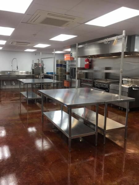 Empty stainless-steel commercial kitchen with tables, shelves, and a glossy red floor