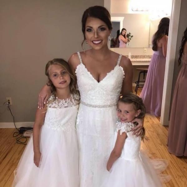 Three people in white dresses smiling indoors, likely at a formal event.