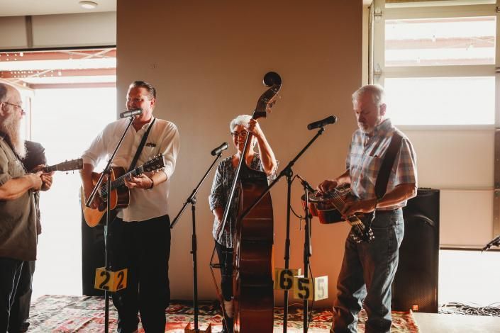 Four musicians performing live indoors with microphones, guitars, and a double bass.