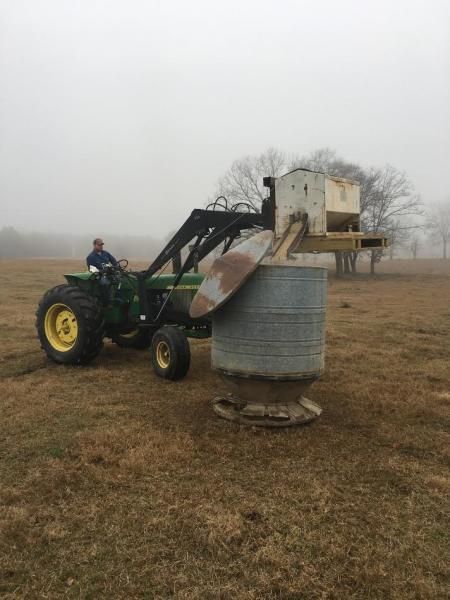 Green tractor lifting a metal bin in a foggy field