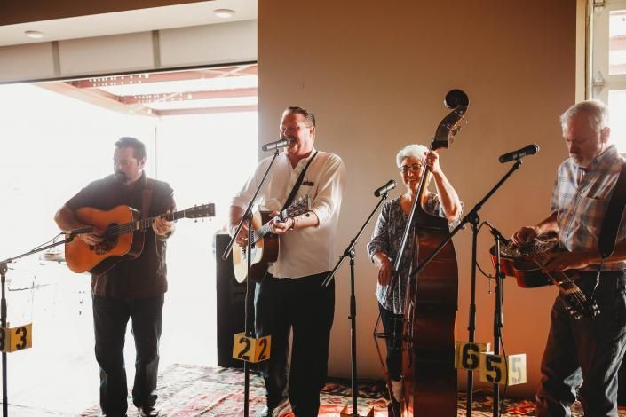 Four musicians perform acoustic folk music onstage with microphones and instruments.