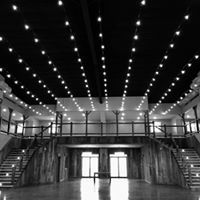 Black-and-white interior of a large hall with string lights, staircases, and balcony railings leading to central doors