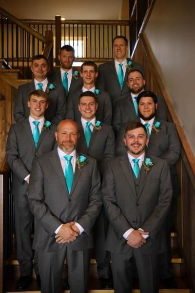 Group of men in gray suits with teal ties posing on a wooden staircase