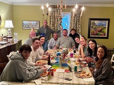 Family gathered around a dining table in a warmly lit room, sharing a meal and posing for a group photo
