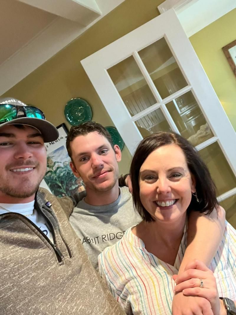 Three smiling people posing together indoors in a bright room with white trim.