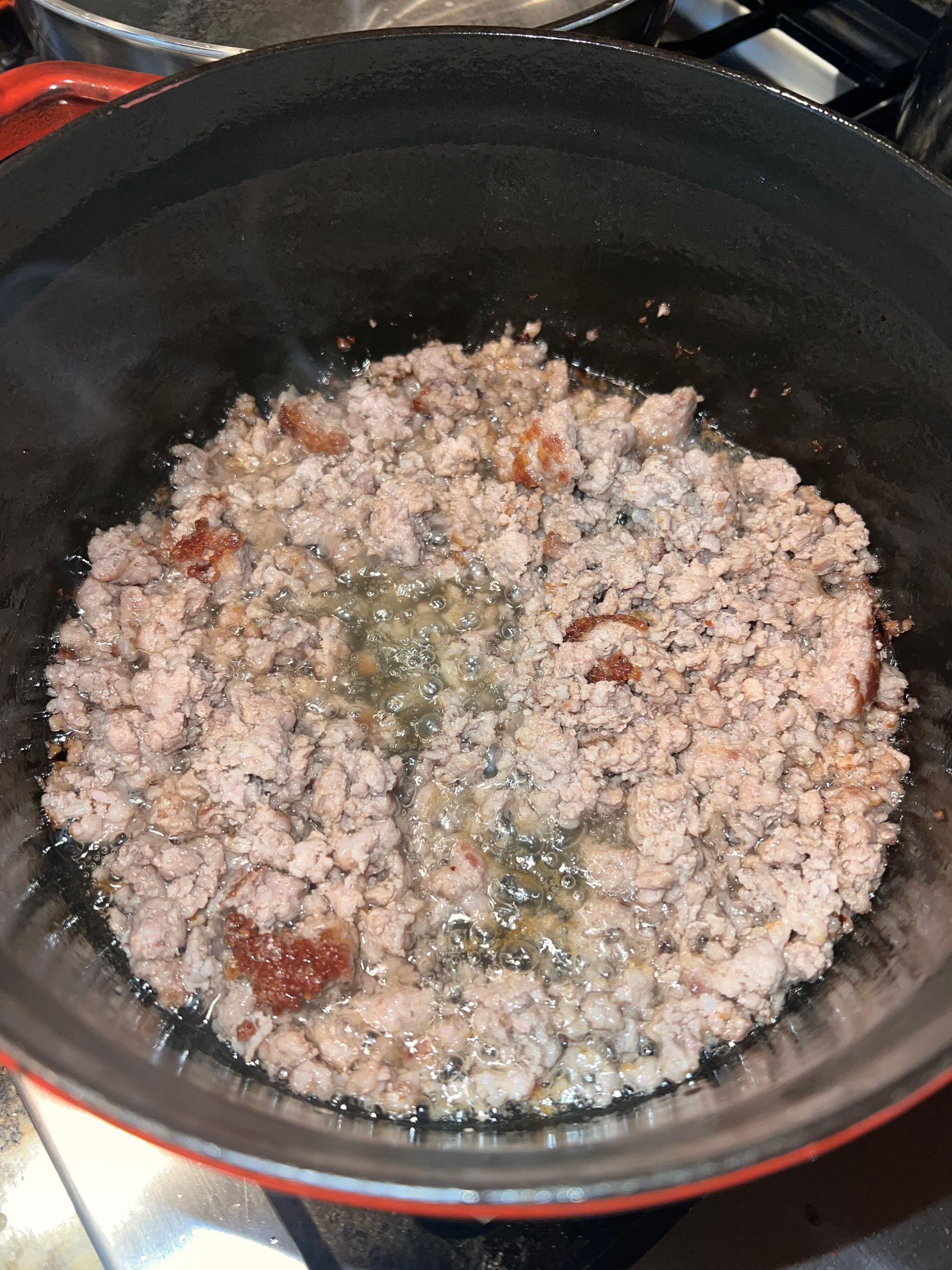 A pot of simmering minced meat with green herbs and tomato pieces on a stovetop