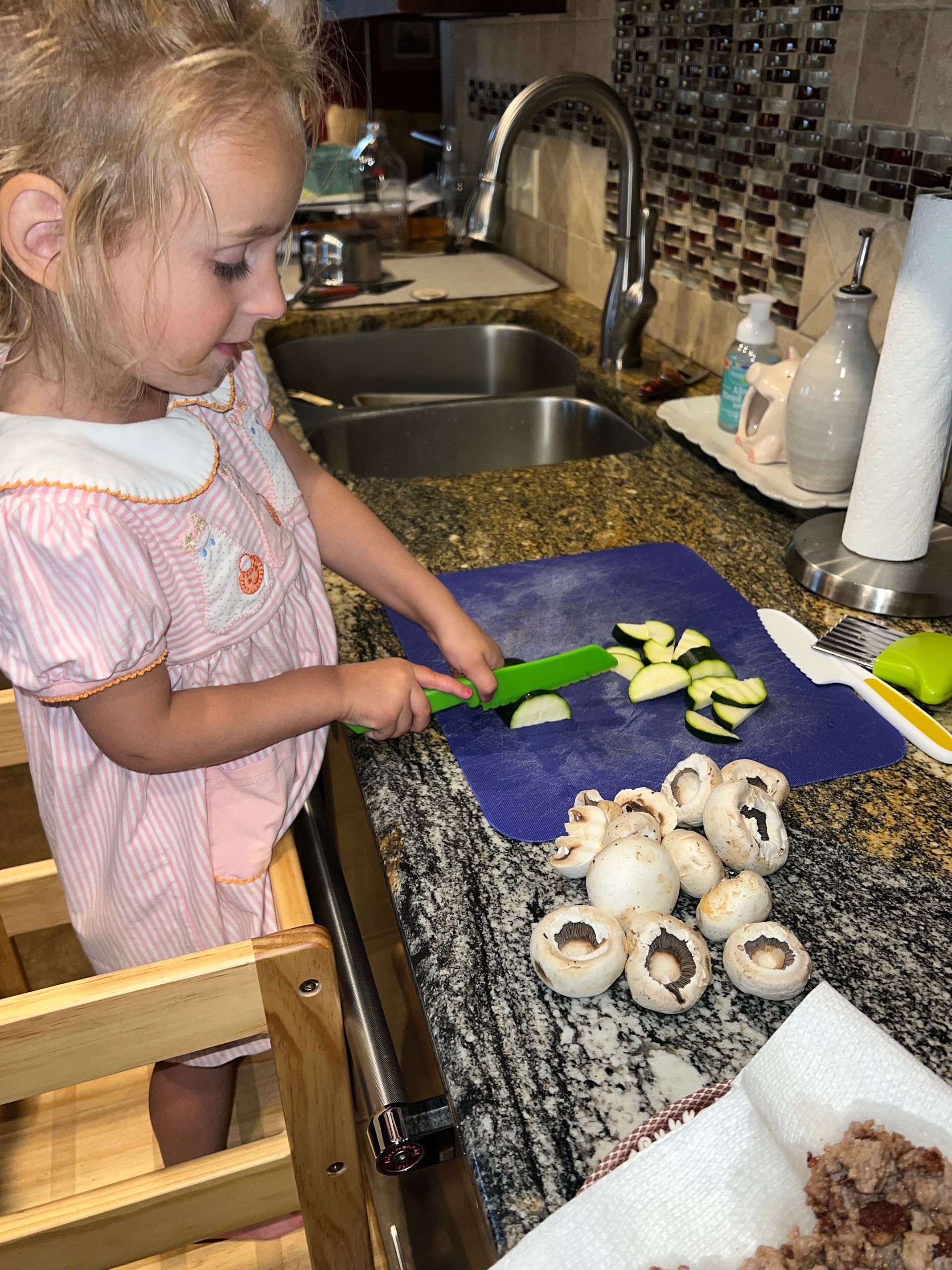 Child slicing zucchini on a blue cutting board beside mushrooms in a kitchen