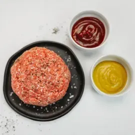 Raw ground meat on a black plate with red and yellow sauces in small bowls nearby