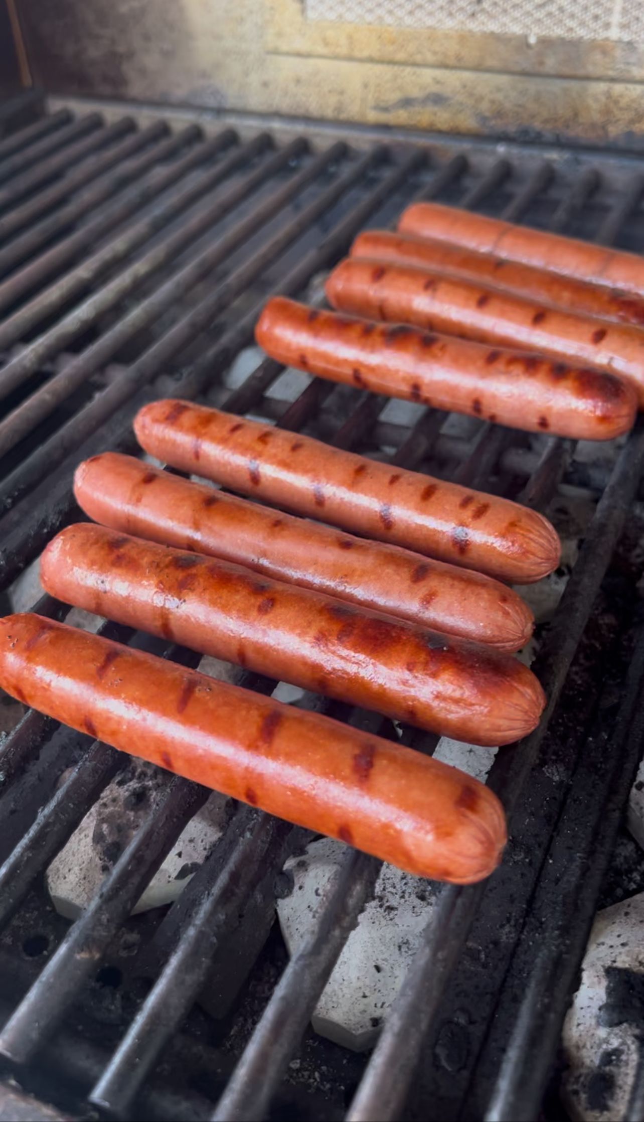 Five hot dogs grilling on black barbecue grates, lightly charred.