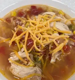 Bowl of soup topped with shredded cheese, chicken slices, beans, and vegetables