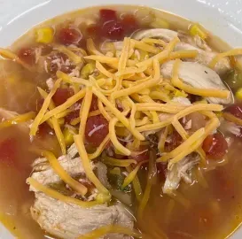 Bowl of chicken soup topped with shredded cheddar, beans, and diced vegetables