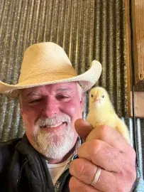 Man in a straw hat holding a yellow chick, smiling indoors