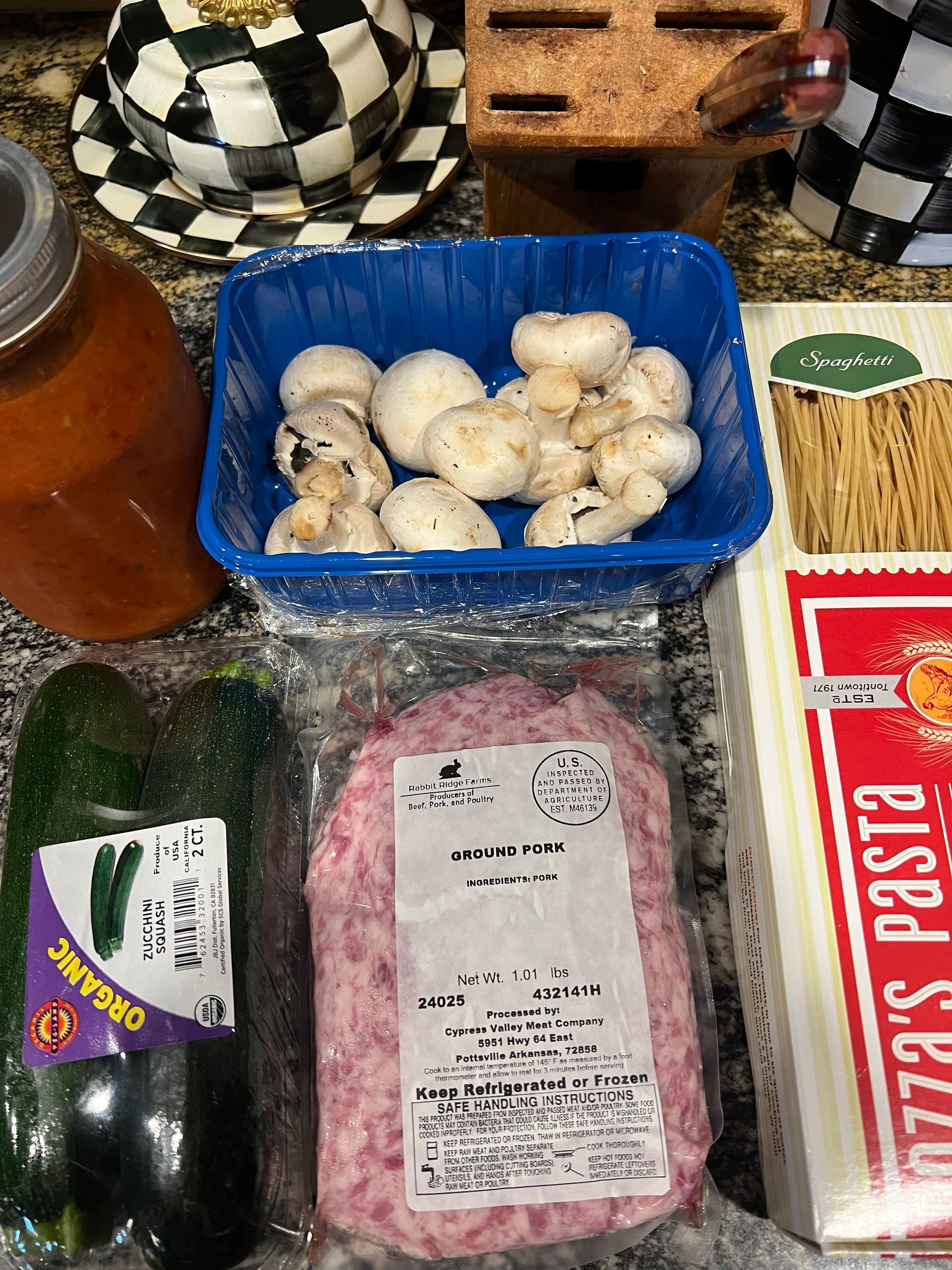 Groceries on a counter: mushrooms, zucchini, pasta, noodles, a jar, and packaged meat.